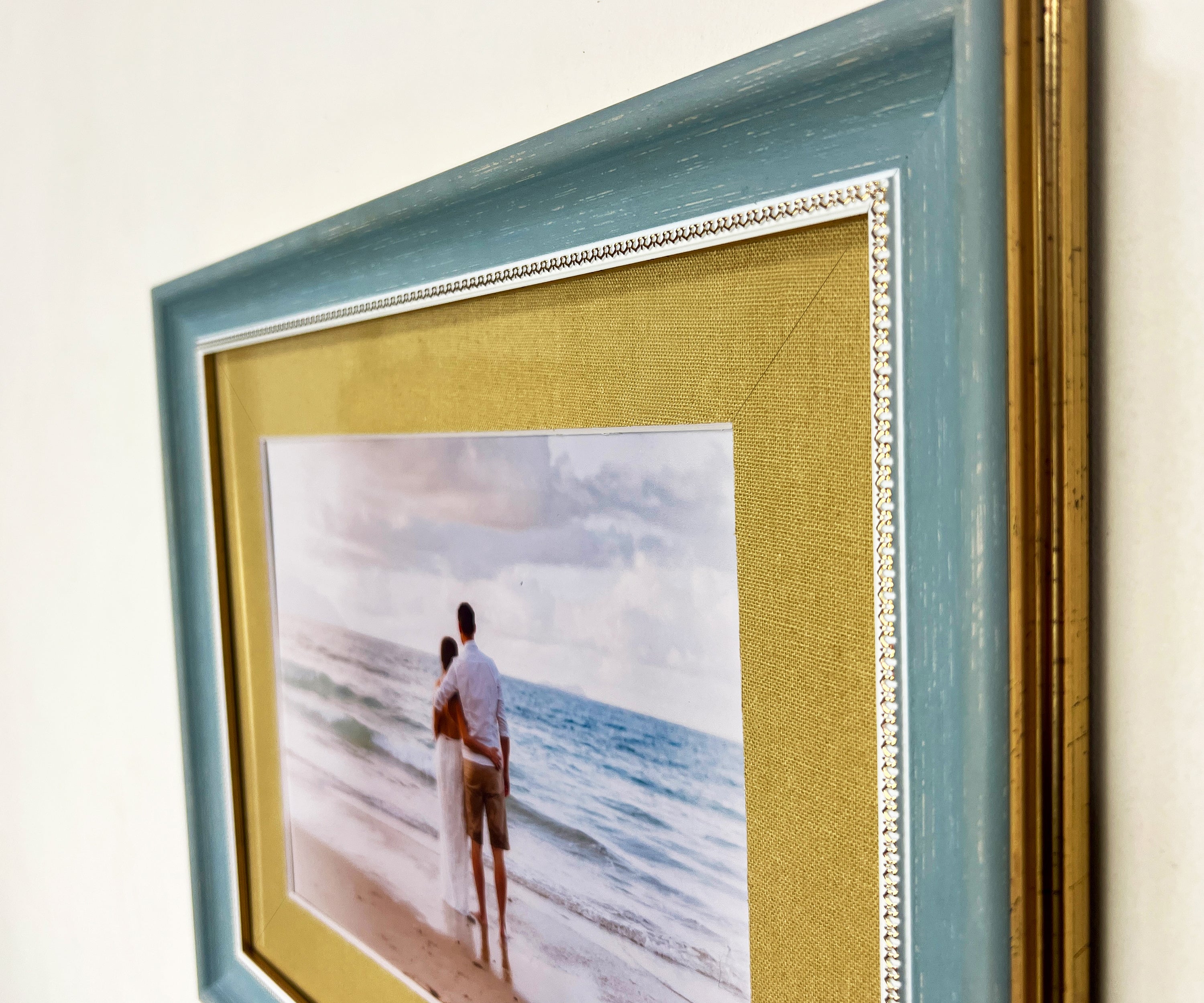 Close-up of elegant blue wooden picture frame with gold matboard and beach photo print.
