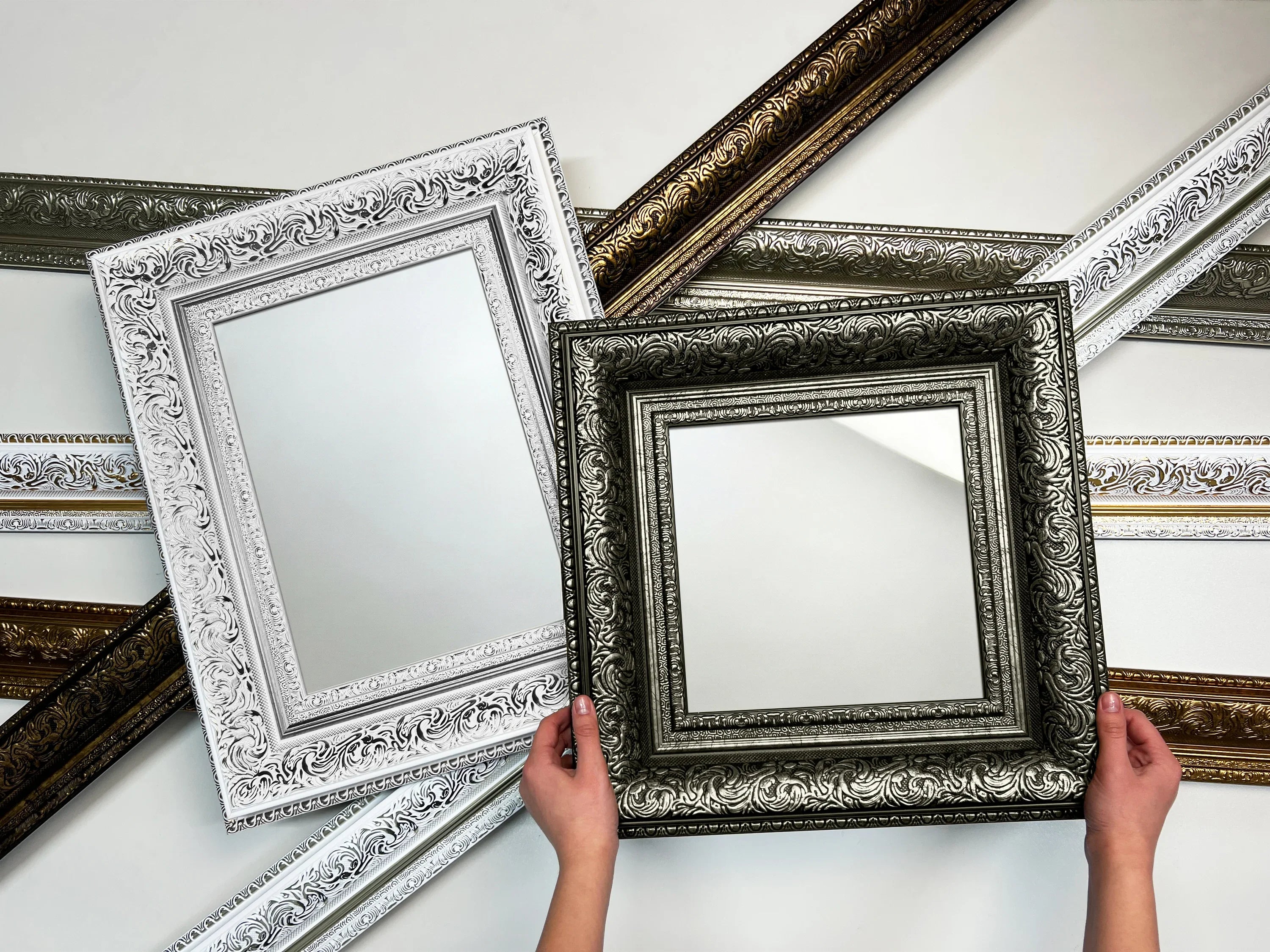 Ornate European-style handcrafted wooden picture frames with intricate detailing, in gold, white, and silver finishes, displayed against a neutral background.