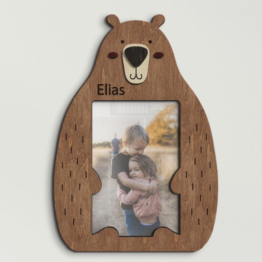 Wooden 4 by 6 inches photo frame in the shape of a cute sitting bear holding a photo. The name is engraved above the photo. This frame is 10 by 7 inches and 8 millimeters thick. The bear can be painted in different colors. The name can be changed.